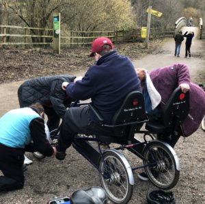Three people helping to set up someone on a trike, at Cannop Cycle Centre by the bridge.