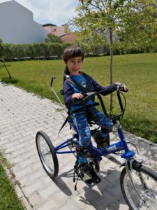 A boy on a blue trike, smiling at the camera.