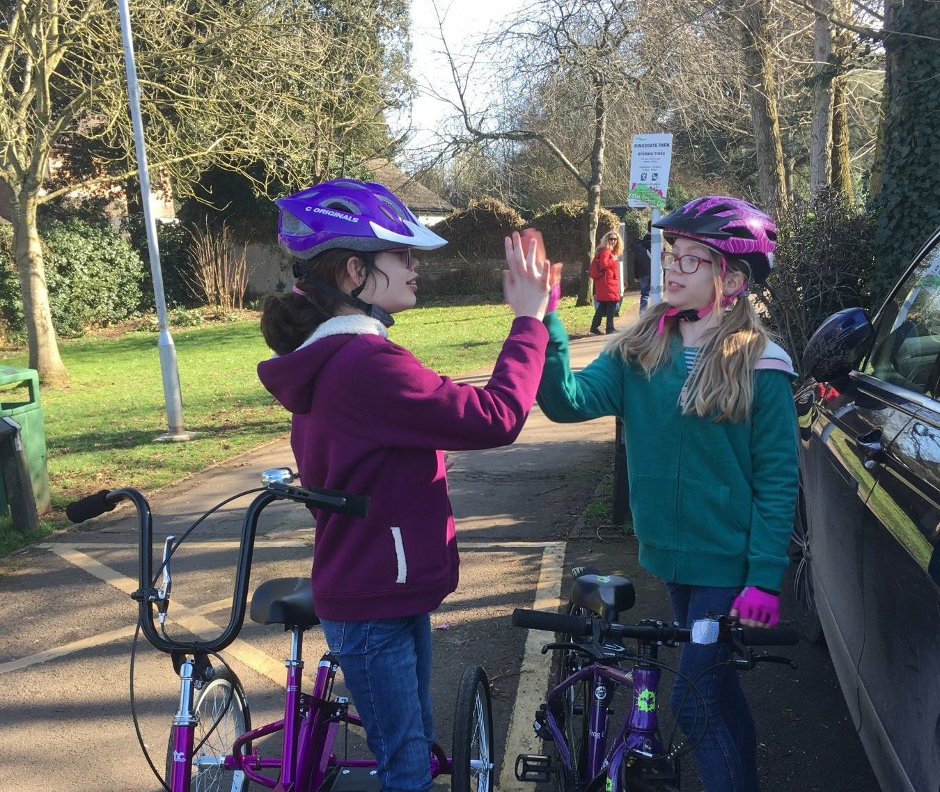 Two children standing astride bikes - one is traditional, one is a Tomcat trike - high-fiving.