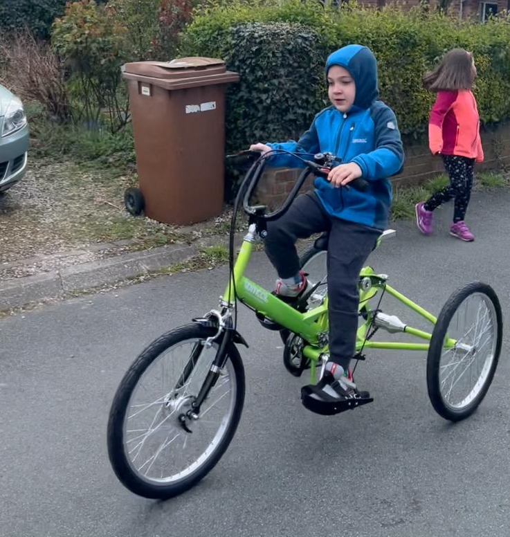 A child riding up the road in the rain on a green Tomcat Roadhog.