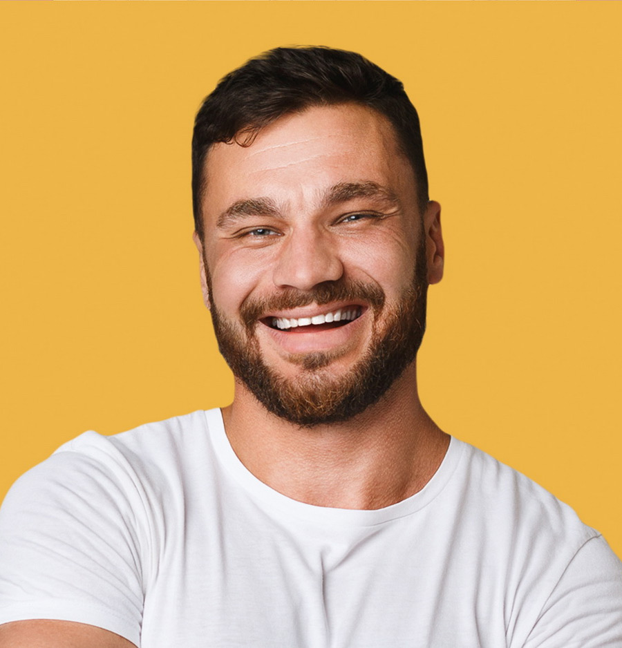 A man in a white shirt on a muted yellow background. He is smiling at the camera.