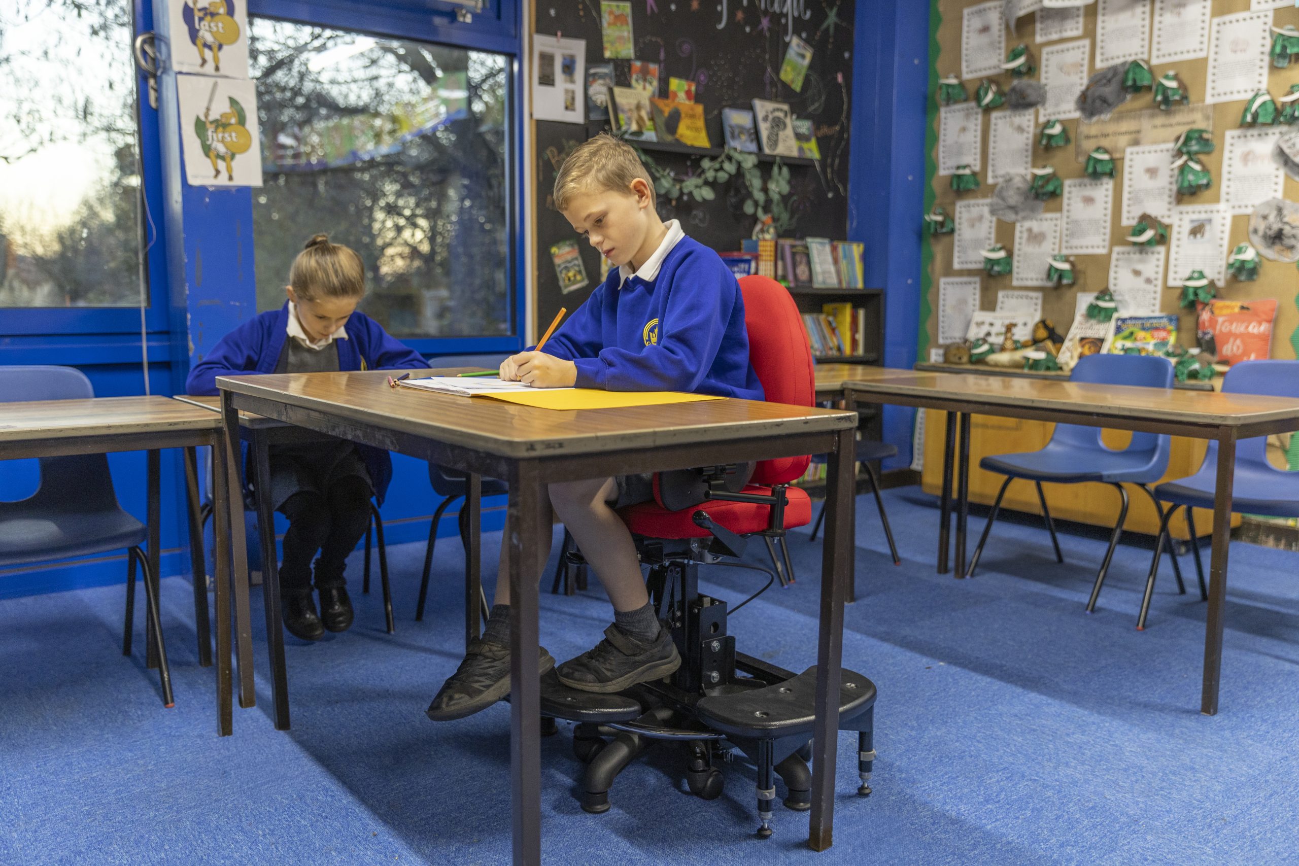 A boy doing his school work in his classroom, while sat on the SoloSeat By Tomcat.