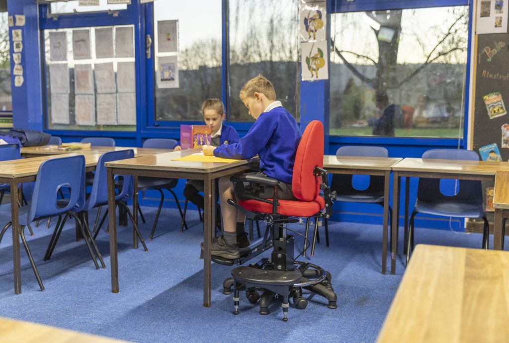 A boy doing his school work in a classroom while sat on the SoloSeat by Tomcat