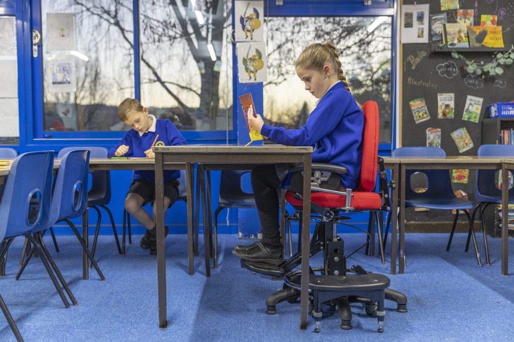 A girl doing her school work in her classroom, while sat on the SoloSeat by Tomcat